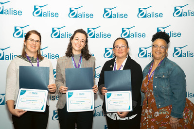 Four women showing their awards at the association for library information science & education conference in portland Oregon in front of a step and repeat