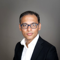 Headshot of an Indian man wearing a white shirt and a black blazer