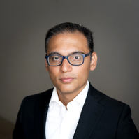 Headshot of an Indian man wearing a white shirt and a black blazer
