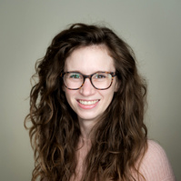 Studio headshot of a young female professional with curly hair and a pink sweater