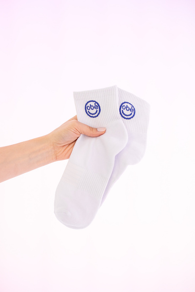 An e-commerce photograph of white athletic socks with a purple logo.