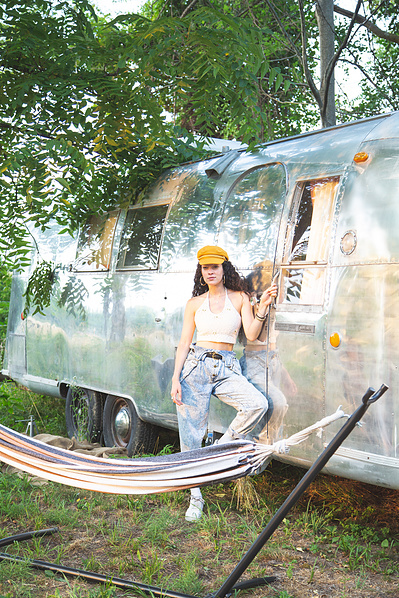 A brunette model posing by an airstream and hammock.