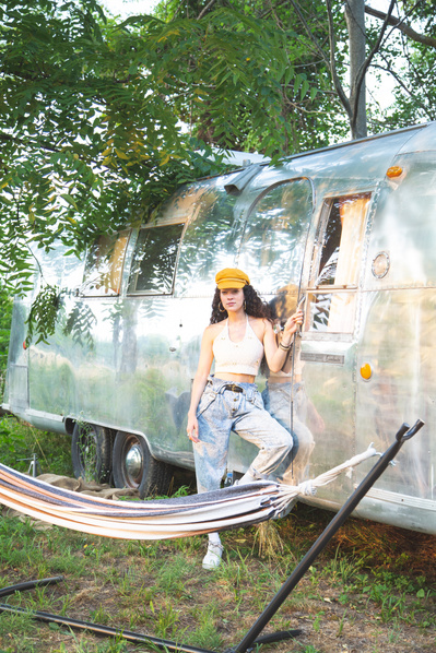 A brunette model posing by an airstream and hammock.