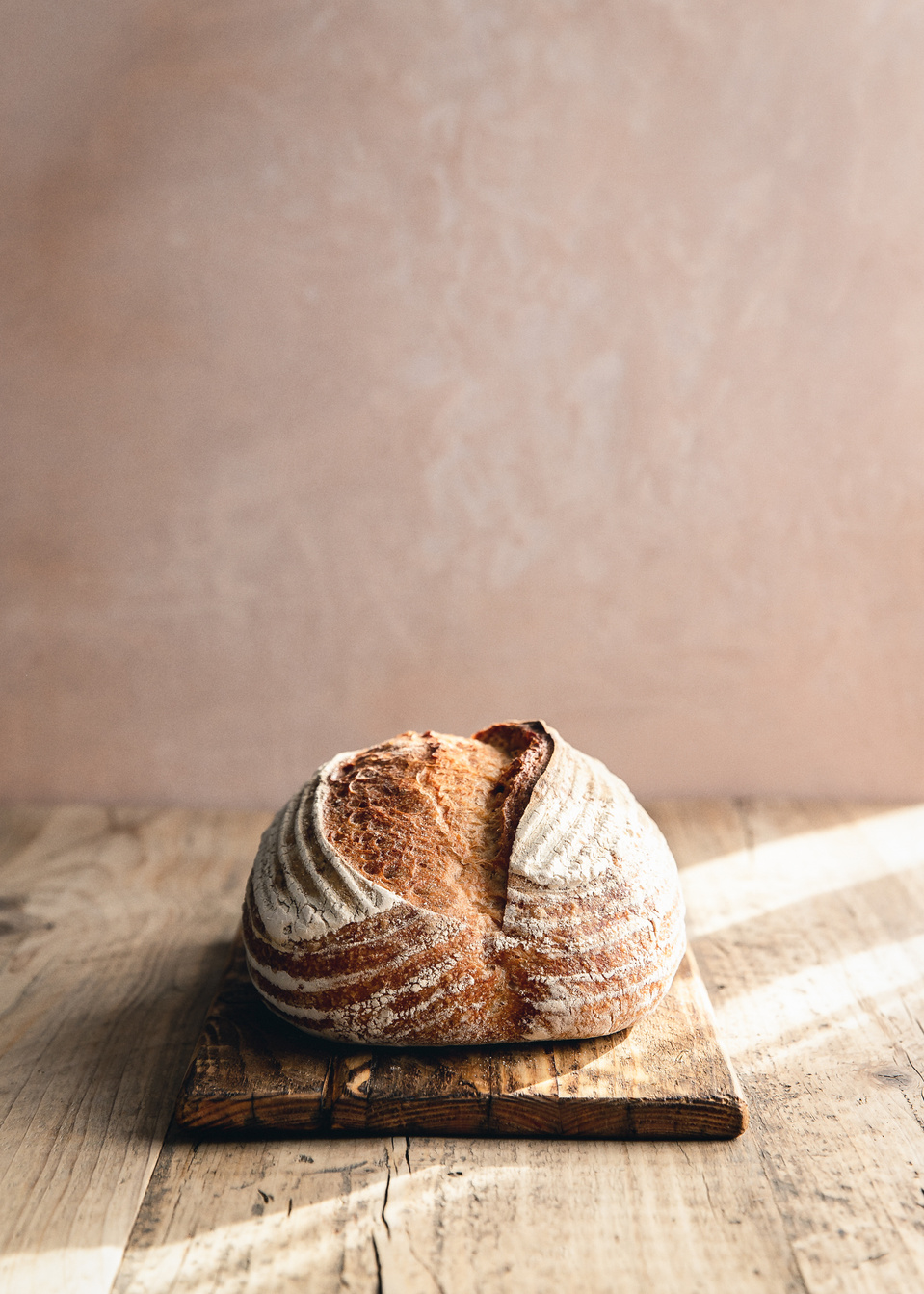 Elise Humphrey - food photographer - loaf of sourdough bread on a wooden chopping board with a pink plaster background