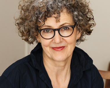 Woman with short curly hair and glasses and deep blue shirt.