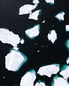 Drone shot from above of three stand up paddlers paddling through a labyrinth of icebergs in Greenland.