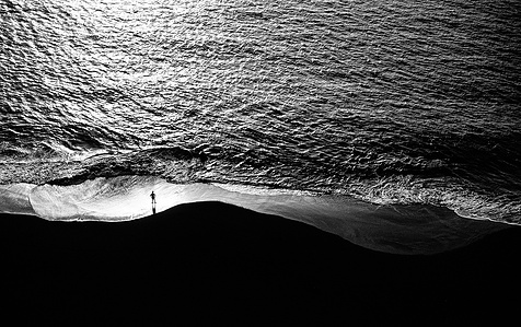 Cape Verdean local standing on a beach and facing the ocean.