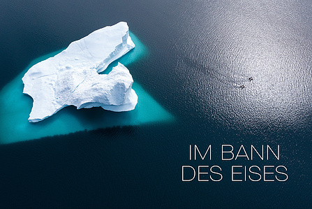 Publication tearsheet of a drone shot from above showing two stand up paddlers paddling on the ocean next to a huge iceberg in north Greenland.