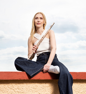Celebrity photography – Flautist sitting on a wall top in front of the sky.