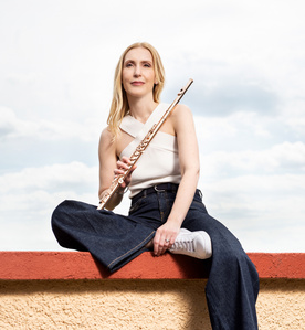 Celebrity photography – Flautist sitting on a wall top in front of the sky.