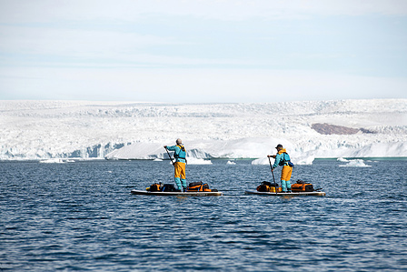 Two stand up paddlers paddling in front of the massive ice sheet in Greenland.