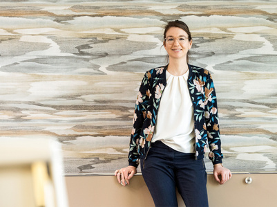 Half body portrait of employee sitting on side board with patterned wall in the back - by Swiss photographer based in Zurich.