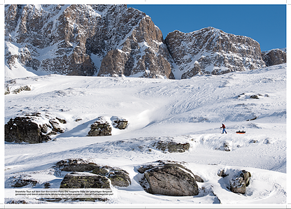 Publication tearsheet of a spread page showing an athlete pulling a sledge on snow in front of impressive mountains at the San Bernardino pass in Switzerland.