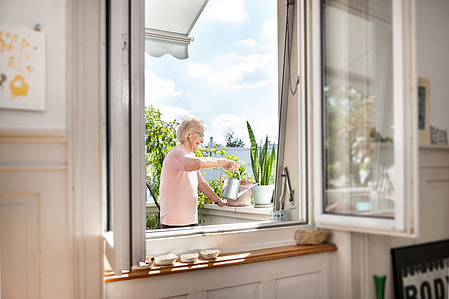 Old woman watering her plant on her balcony.