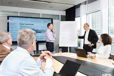 Corporate meeting with 2 employees standing next to a flipchart.