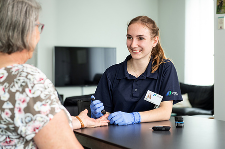 Senior taking her medication in discussion with Spitex employee.