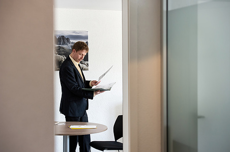 Employee standing in office and looking at documents – corporate reportage.