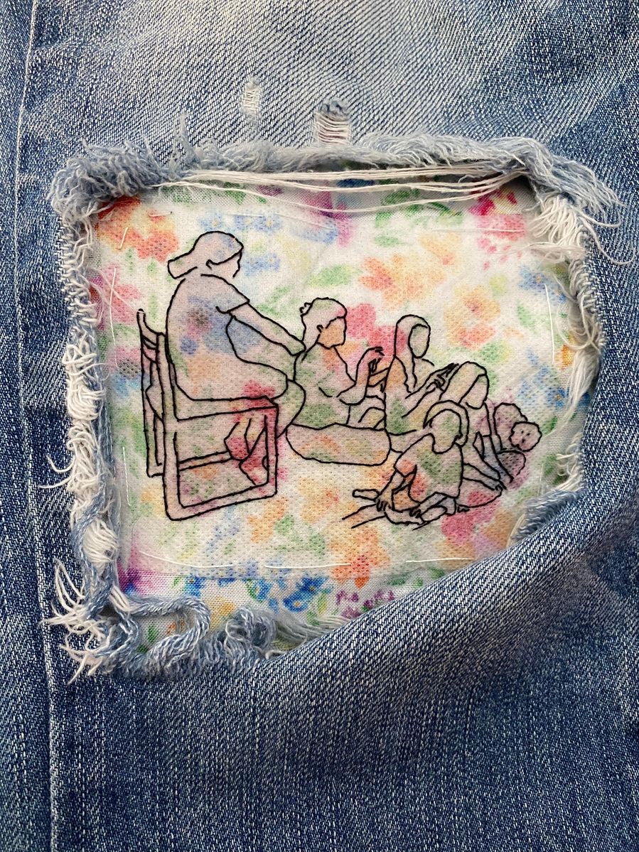 large hole in knee of blue jeans shows an embroidery of 5 little girls and a small fluffy dog, one girl sitting on a chair and the rest sitting on the floor. The first three are sitting in a line each girl braiding the hair of the girl in front of her.