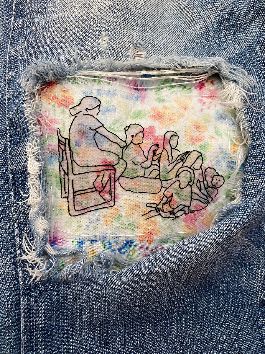 large hole in knee of blue jeans shows an embroidery of 5 little girls and a small fluffy dog, one girl sitting on a chair and the rest sitting on the floor. The first three are sitting in a line each girl braiding the hair of the girl in front of her.