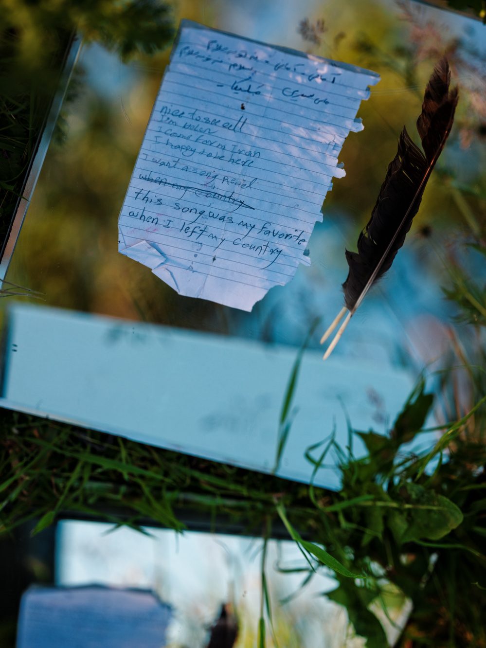 Photograph of a mirrored surface with a feather and a personal handwritten note on it.