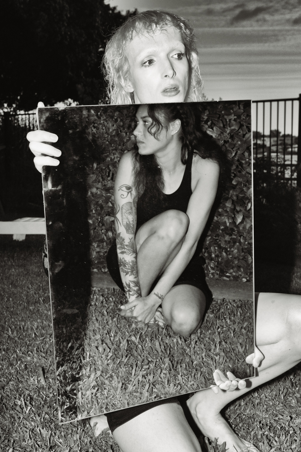 Black and white photograph of a male model holding a mirror reflecting a female model.