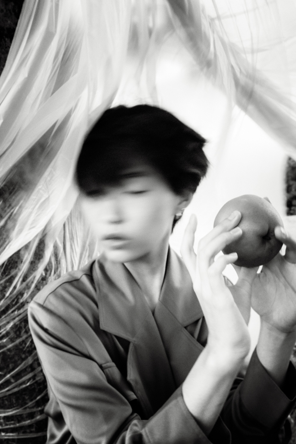 Black and white photograph of a female Korean model shaking her head and holding a pear in her hands.