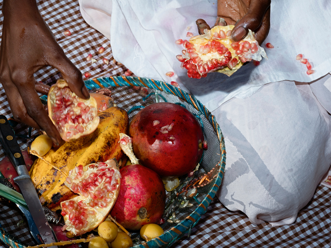 Close-up photograph of a black woman's hands picking an opened pomegranate.
