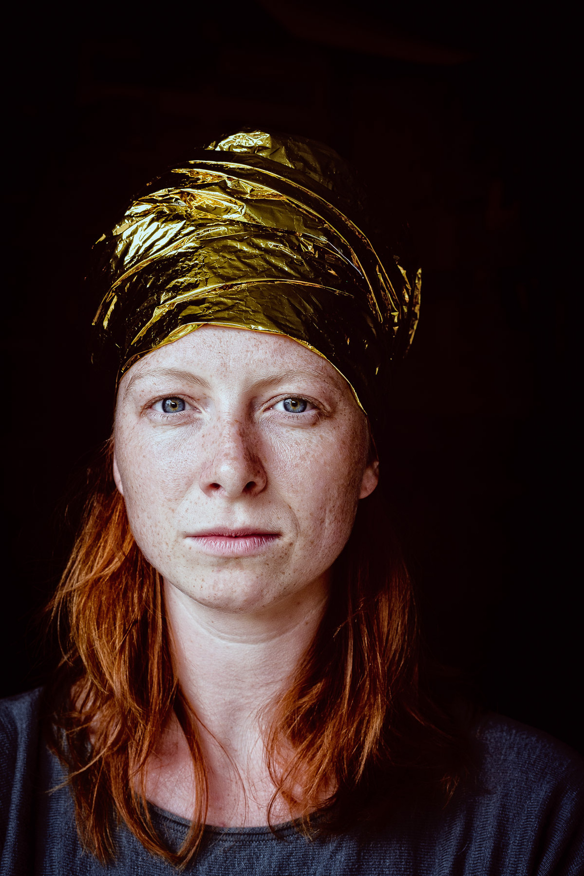 Colour photograph of a young woman with a gold foil headdress looking into the camera.