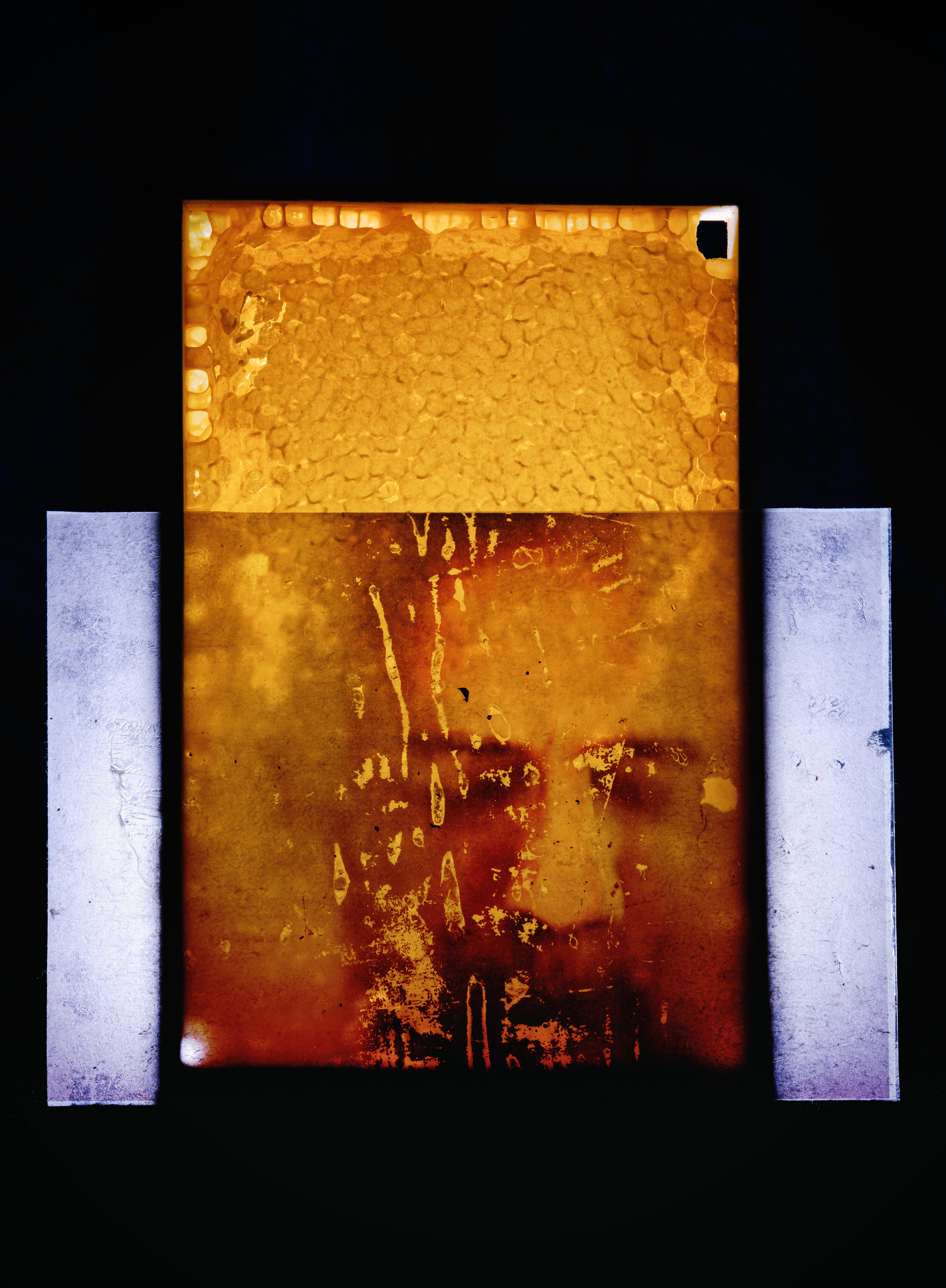 Colour reproduction image of an assemblage including a honeycomb and plastic acetate sheet with a face printed on it.