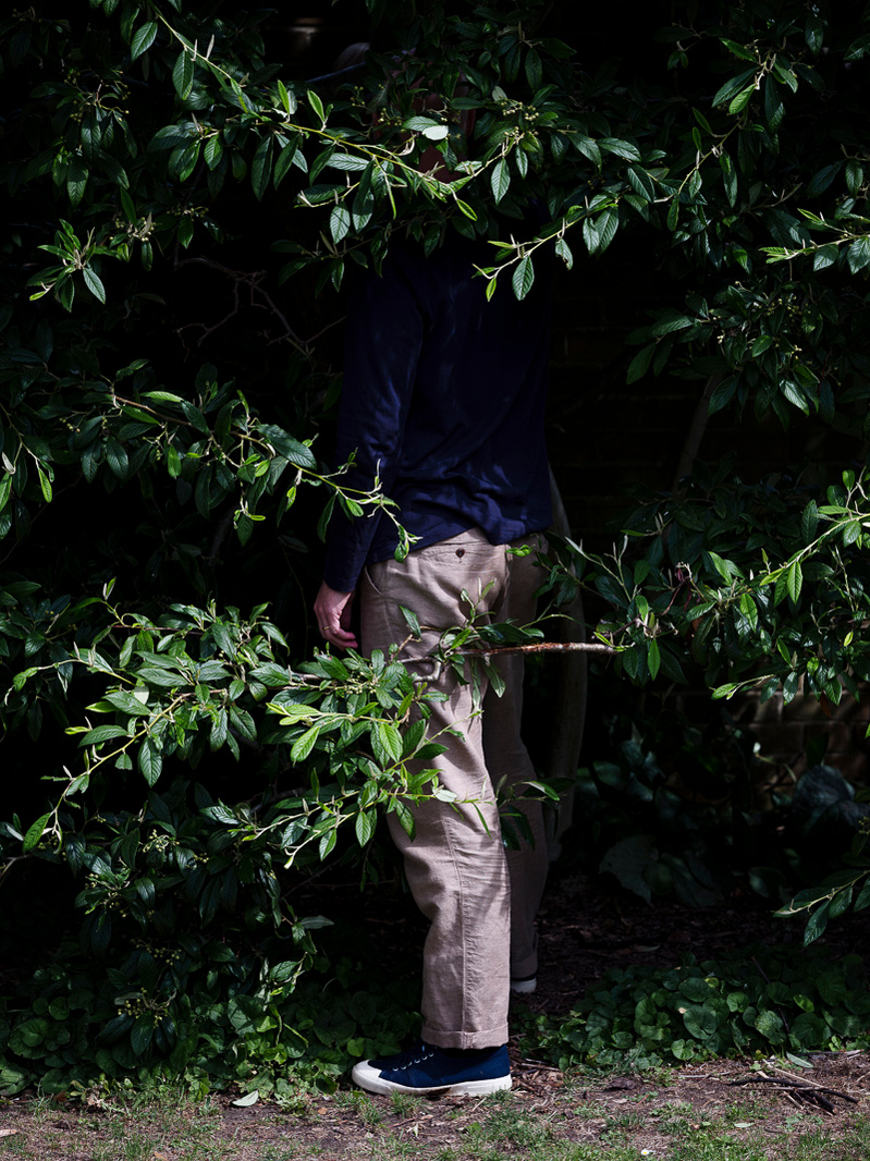 Colour photograph of a man's trousered leg partly obscured by the foliage of a tree.