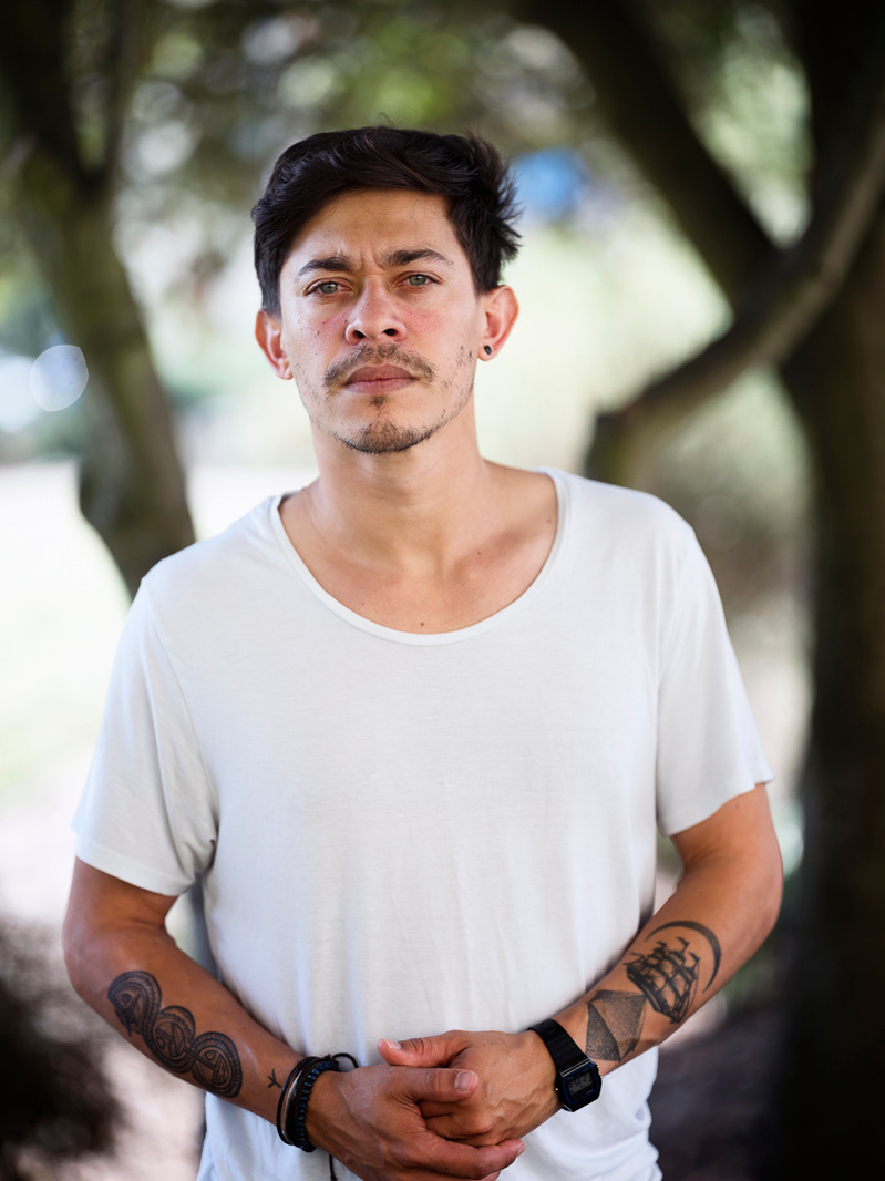 Colour portrait photograph of a male model wearing a white t-shirt looking at the camera with trees in the background.