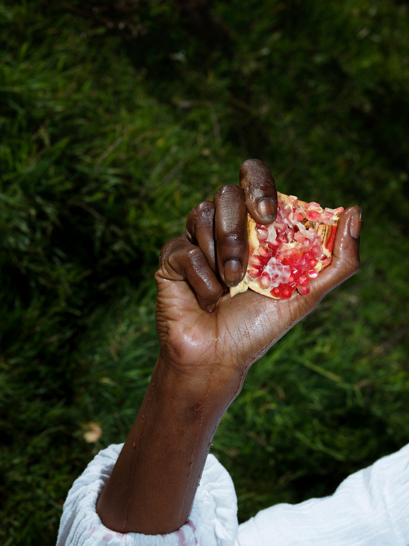 Close-up photograph of a black woman's hand holding an opened pomegranate.