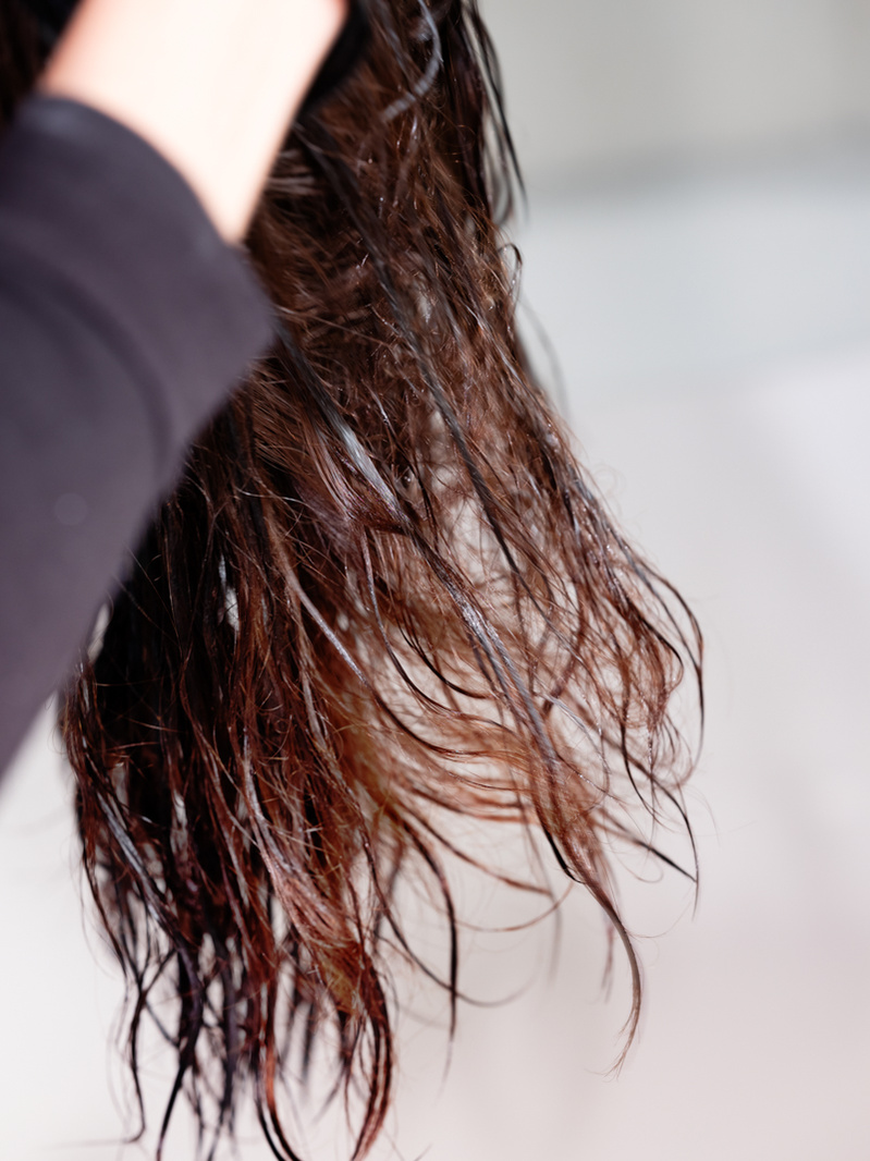 Colour photograph close-up of dark brown hair being dyed by hand.
