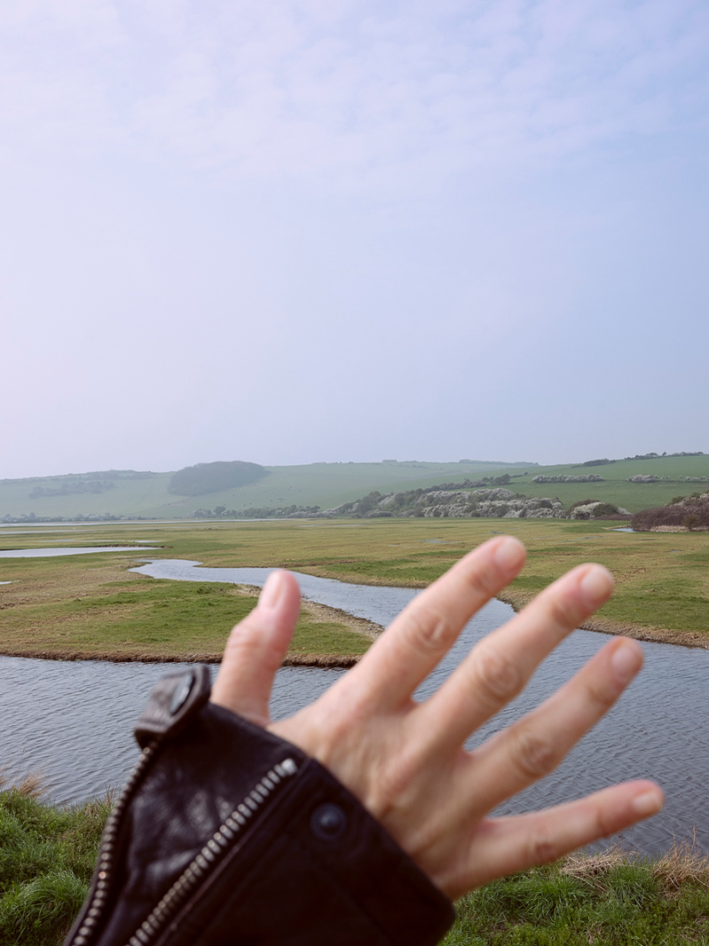Colour photograph of a hand close to the camera with a river landscape beyond it.