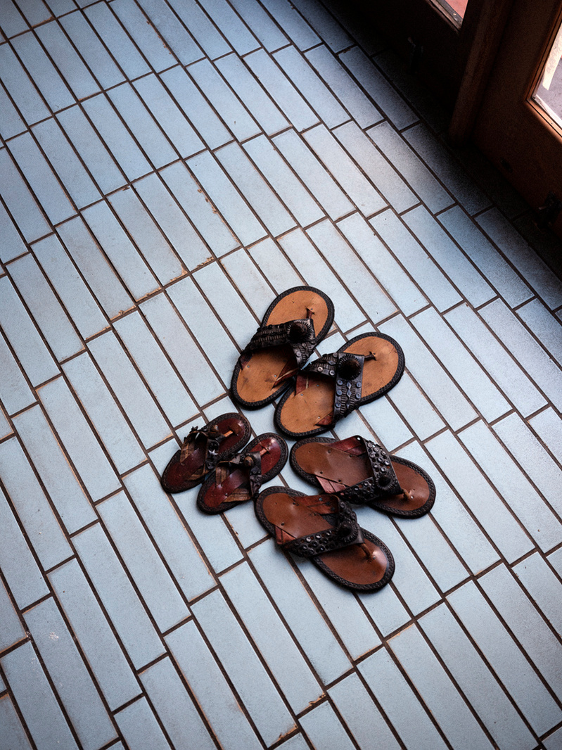 Colour photograph of worn leather sandals on a blue tiled floor.