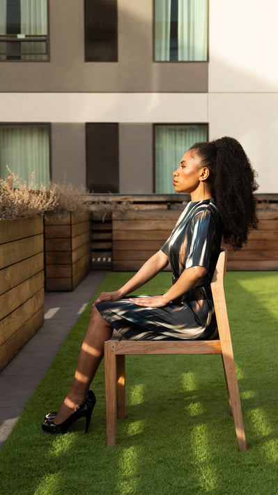 Lifestyle fashion model seated in chair situated profile to camera on hotel rooftop.