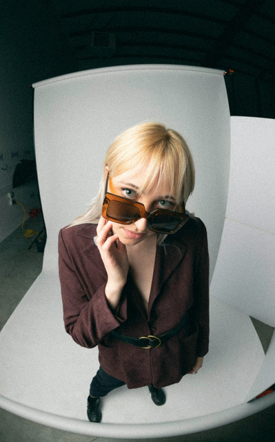 Editorial fashion model in burgundy blazer and sunglasses against white backdrop posing and looking up at camera.