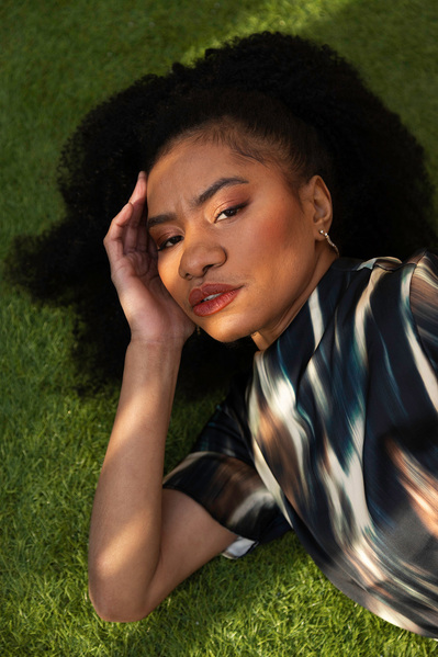 Lifestyle fashion model lays on astroturf in the shade with sun spots shining on her face.