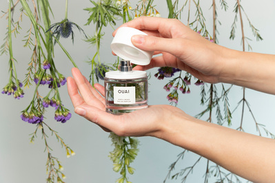 Ouai fragrance product photo of model opening bottle in front of hanging fresh floral backdrop.