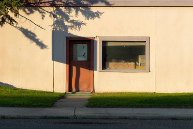 Tired storefront with a red door and window in high contrast sunlight and shadow.