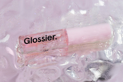 Glossier Lip Gloss product shot covered in gloss on metallic tabletop. 