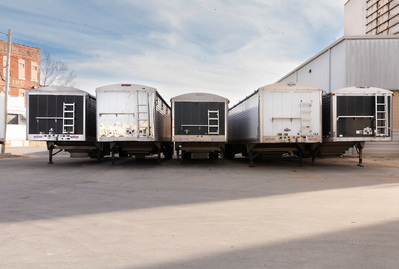 Five alternating black and white tractor trailers parked next to each other.