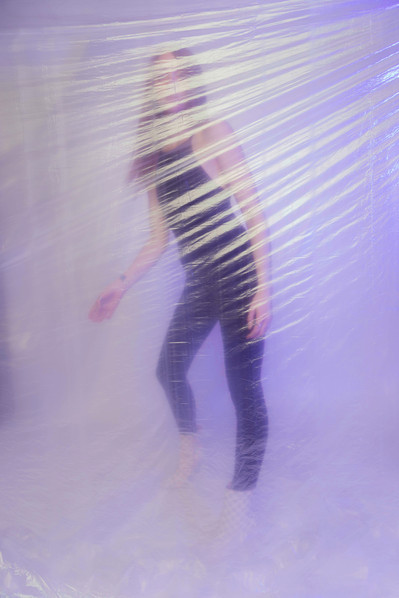 Editorial fashion model in all black posing behind a purple-tinted plastic material.