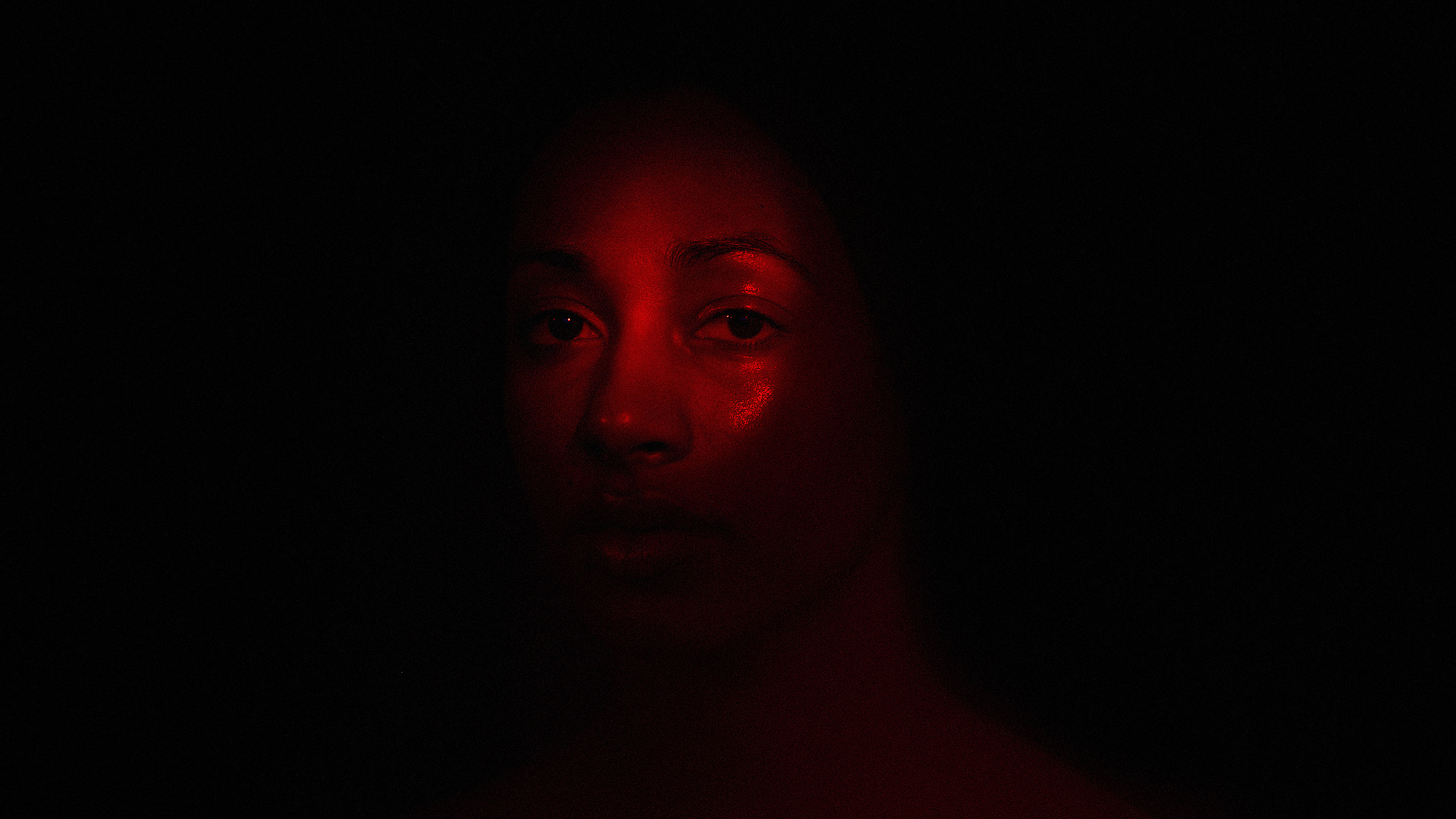 Portrait of a black woman under red light looking at the viewer in front of a black background.