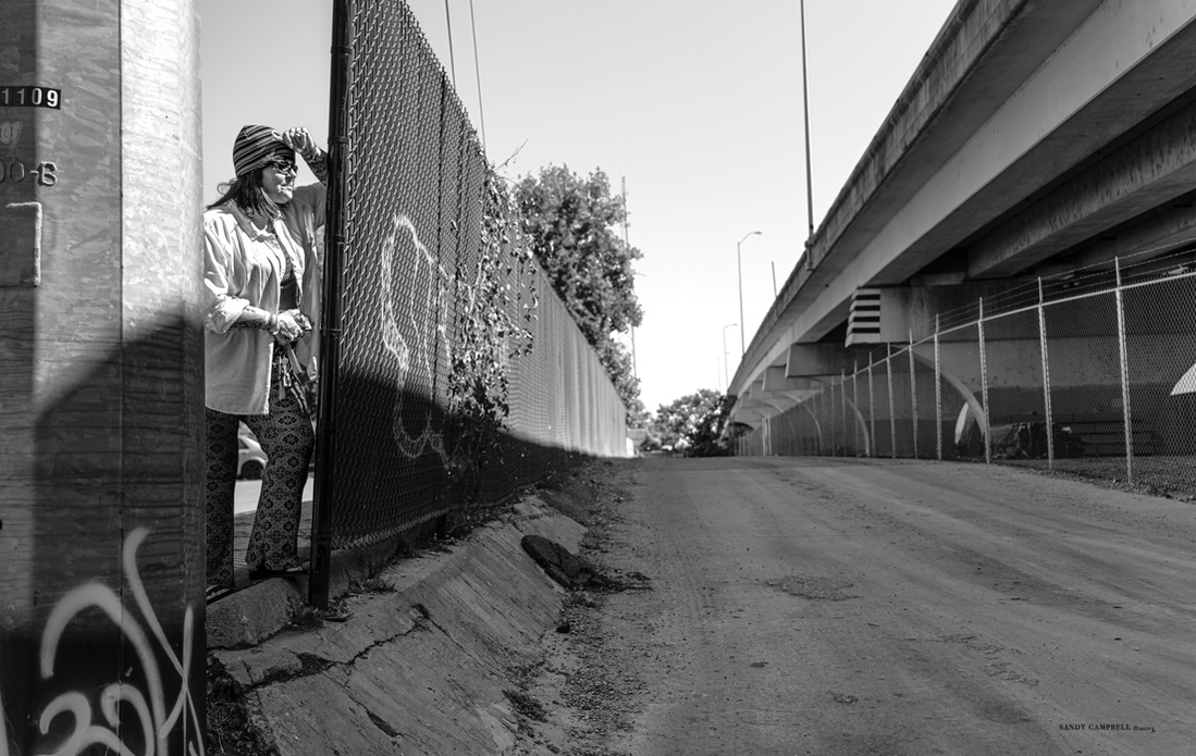 Kimberly revisits the site of her former homeless encampment under a bridge, now enclosed by a fence.