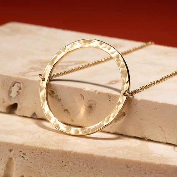Gold circular necklace product photography. It is leaning against beige tiles, with a red background.