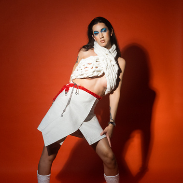 A woman stands in front of an orange studio background dressed in all white.