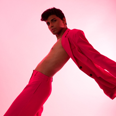 A male model on a magenta background in a full pink suit