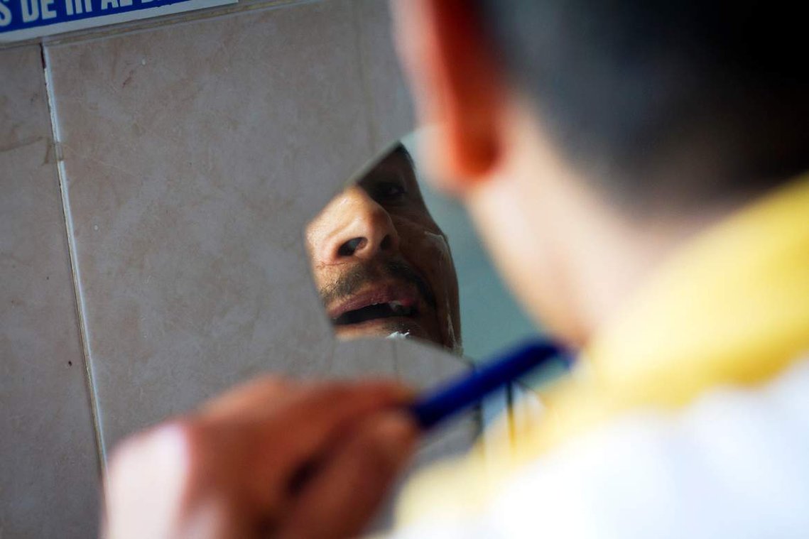 Rodriguez shaves his face using a broken mirror in the men's restroom at Albergue San Juan Bosco. Rodriguez was a welder in Tecate and said he had family there he could live with, but he chose to stay at shelter to fight his case against Border Patrol. 