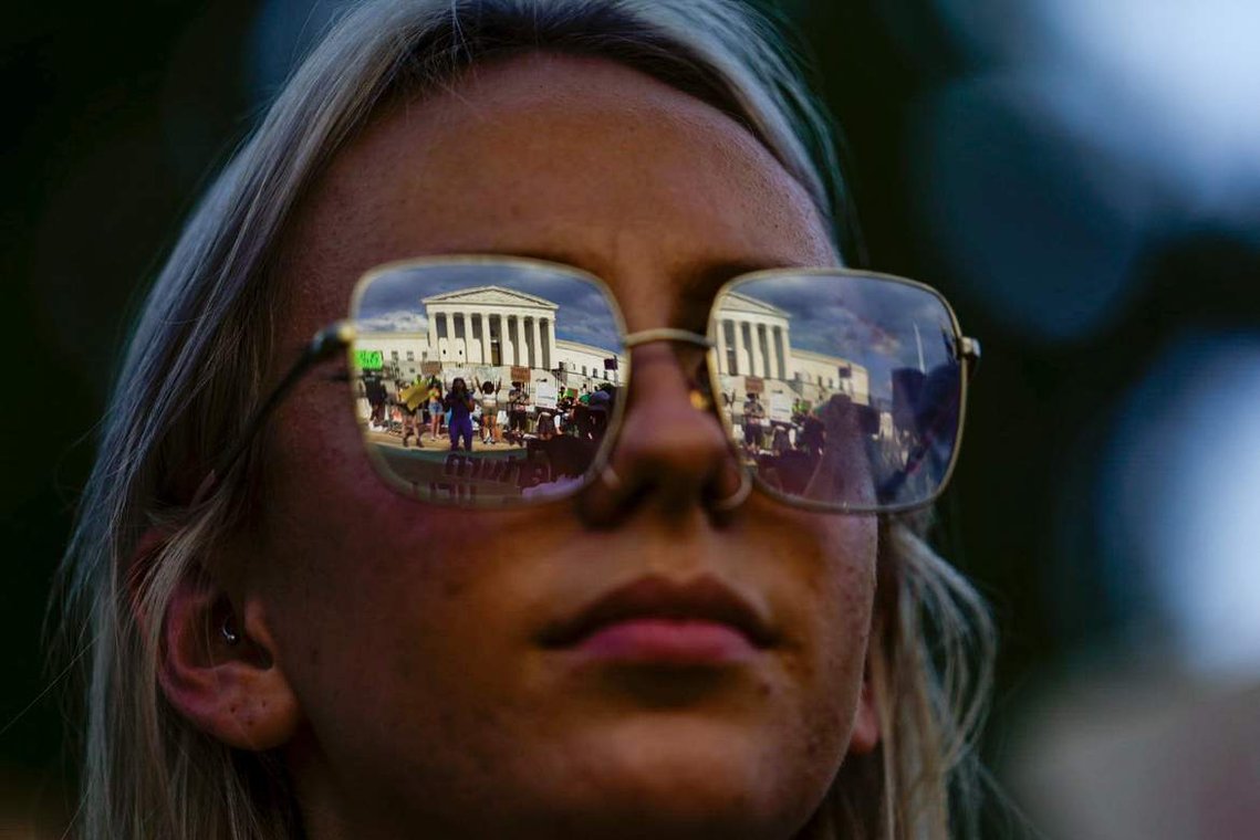 The Supreme Court building is reflected off of Rachel Jakovac's glasses as she participates in a rally Saturday, June 25, 2022, the day after the court's ruling on Dobbs v. Jackson Women's Health Organization.
